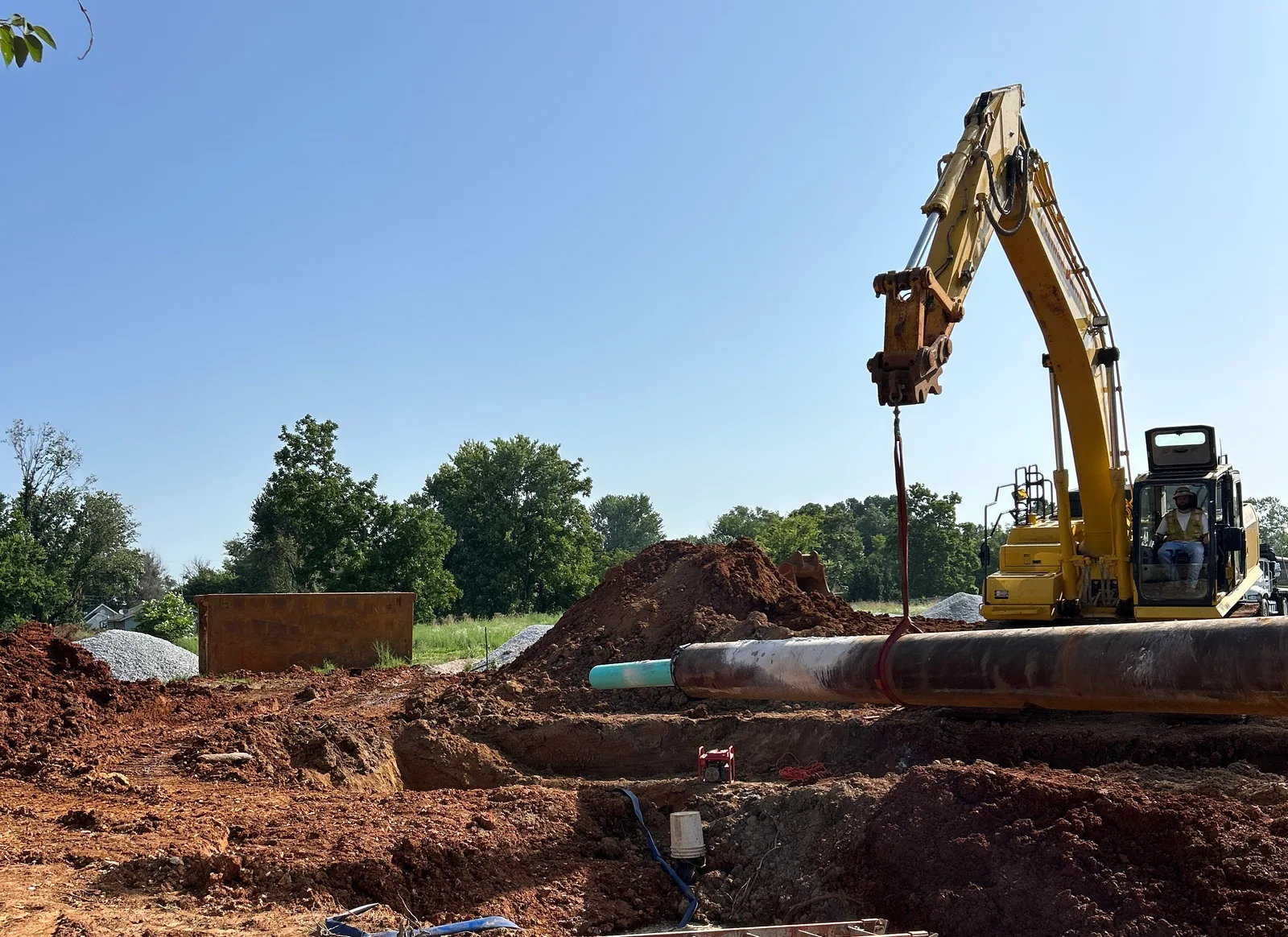 Excavator lifting a utility pipe beside freshly dug ground before building work
